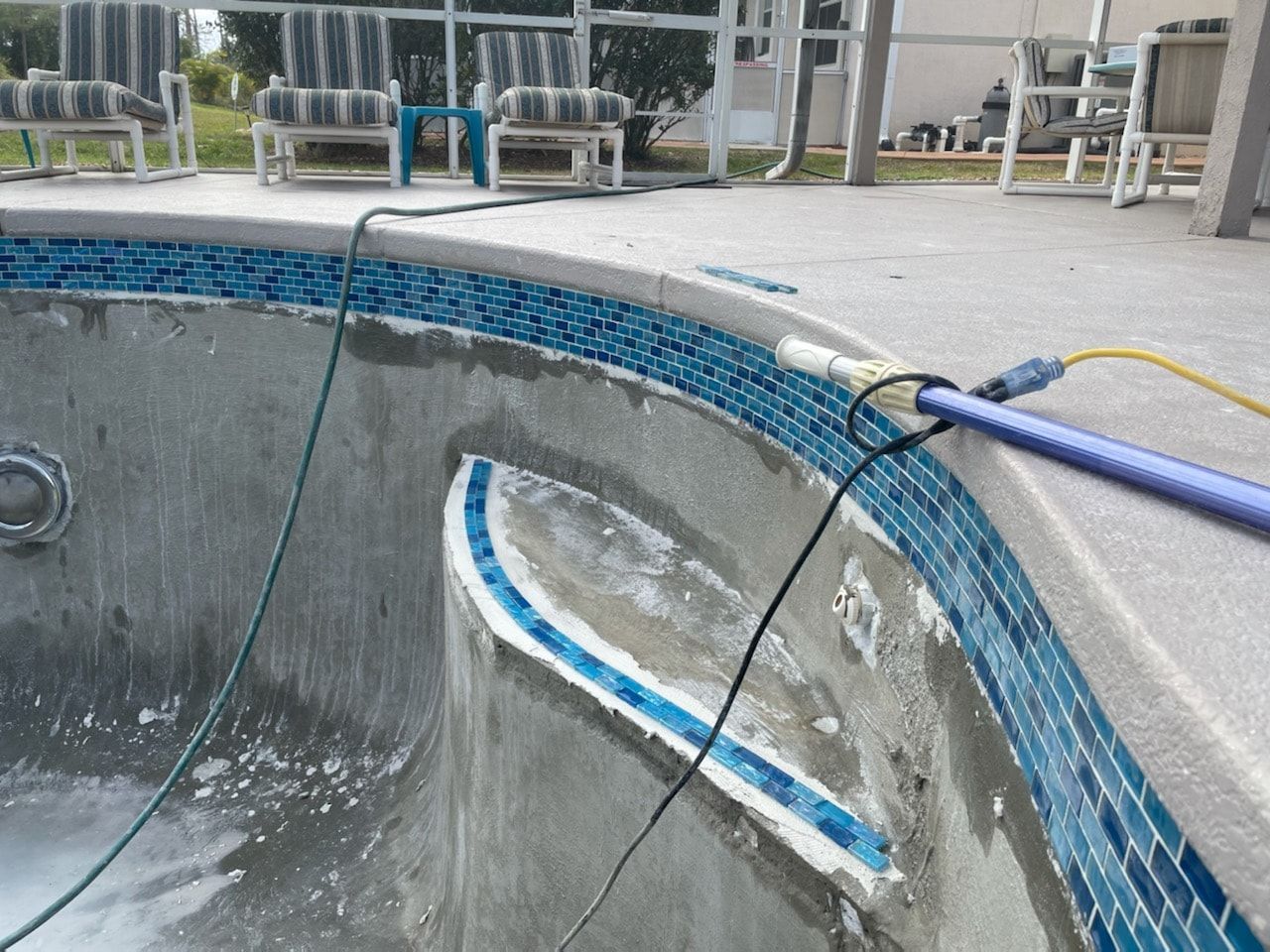 Partially drained swimming pool with blue tile border and cleaning equipment.