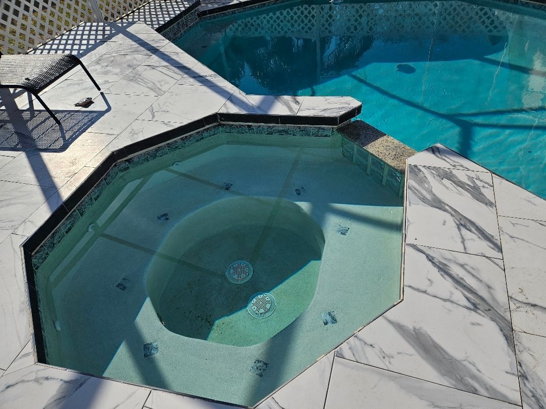 Octagonal spa with teal water next to a rectangular pool. White tile deck, black trim.