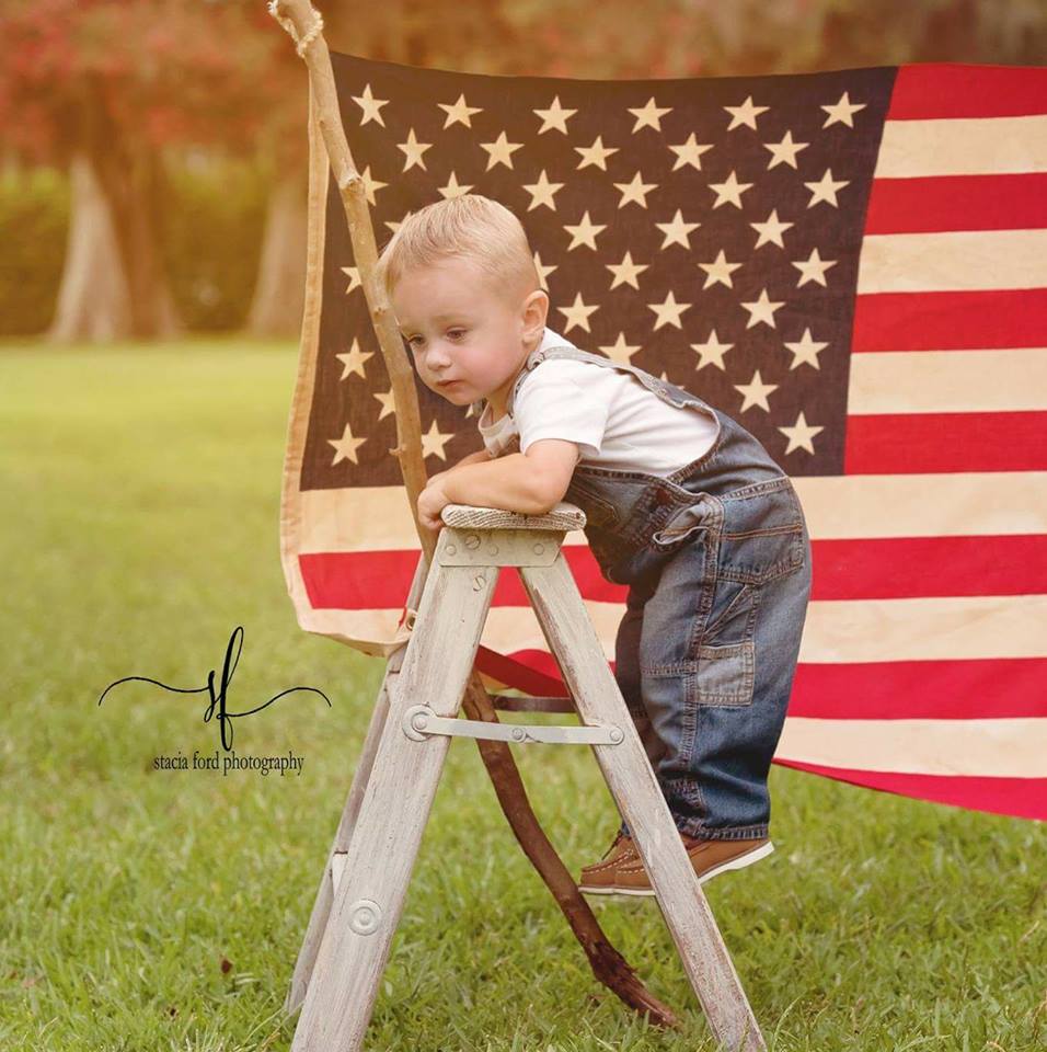 A little boy is standing on a ladder in front of an american flag