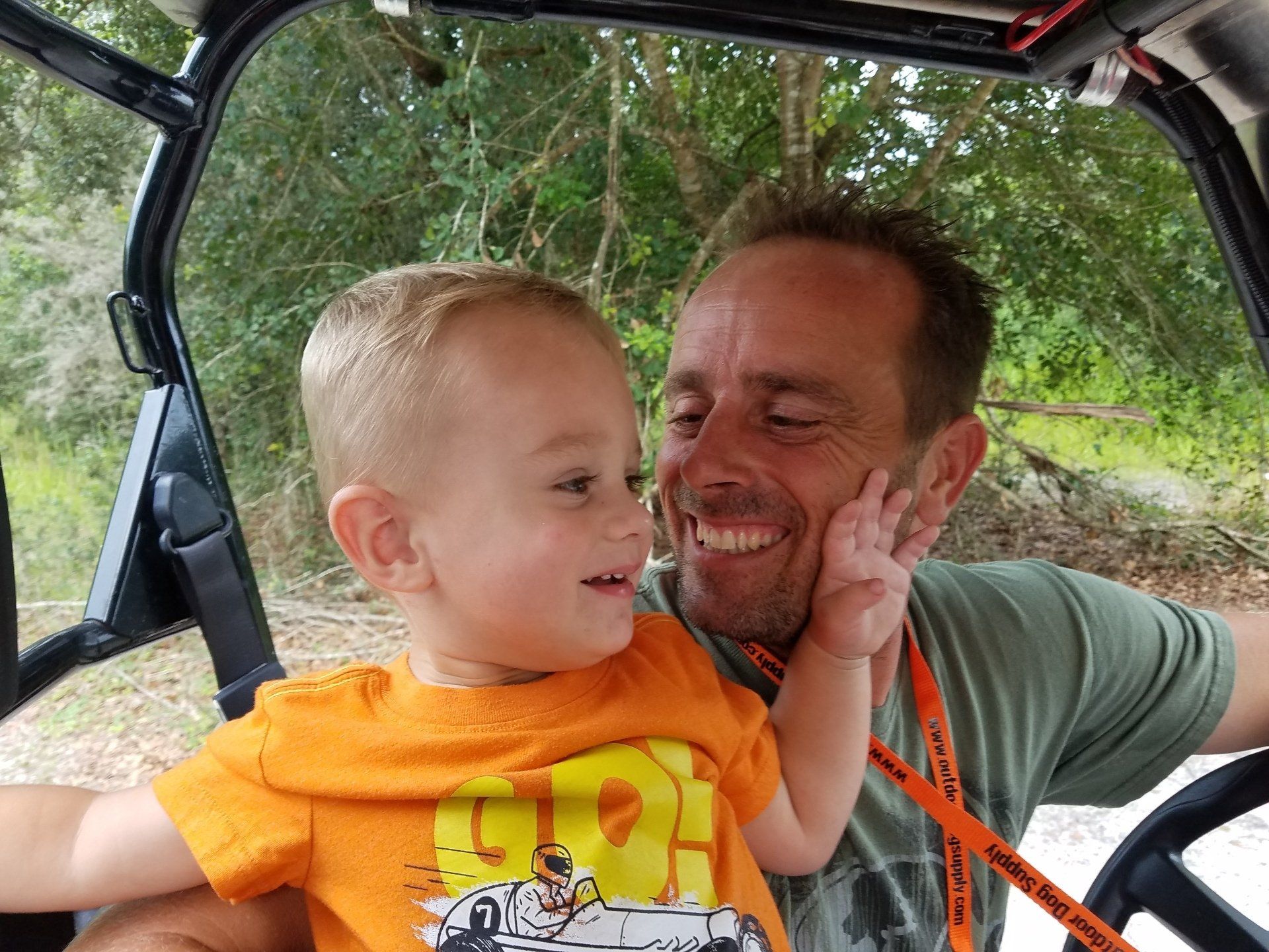 A man is holding a little boy in his arms while sitting in a vehicle.