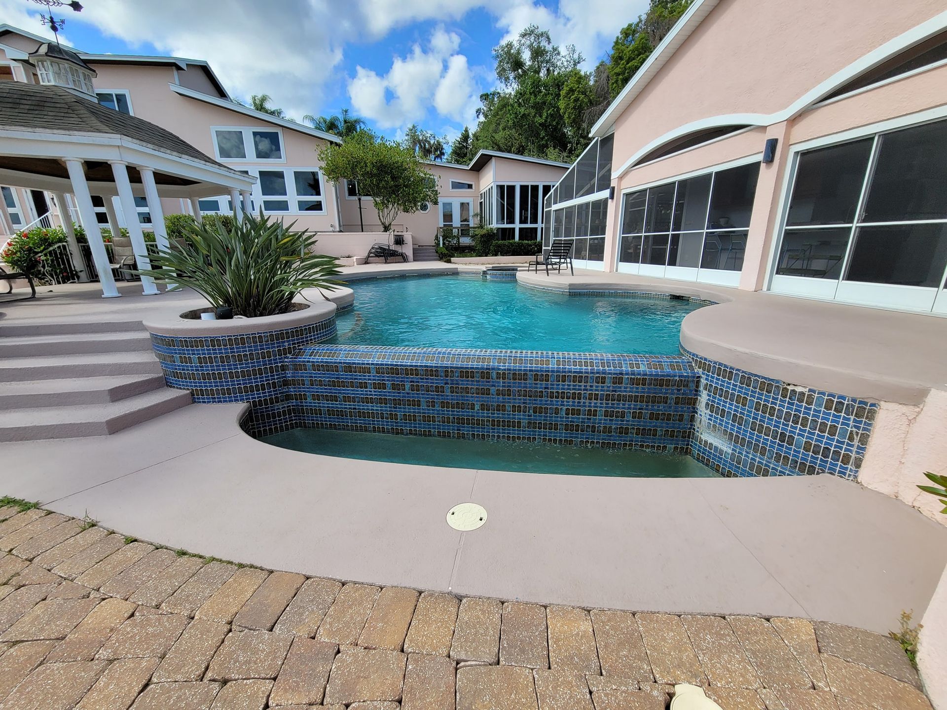Pool with waterfall, surrounded by pink buildings, gazebo, and blue sky.