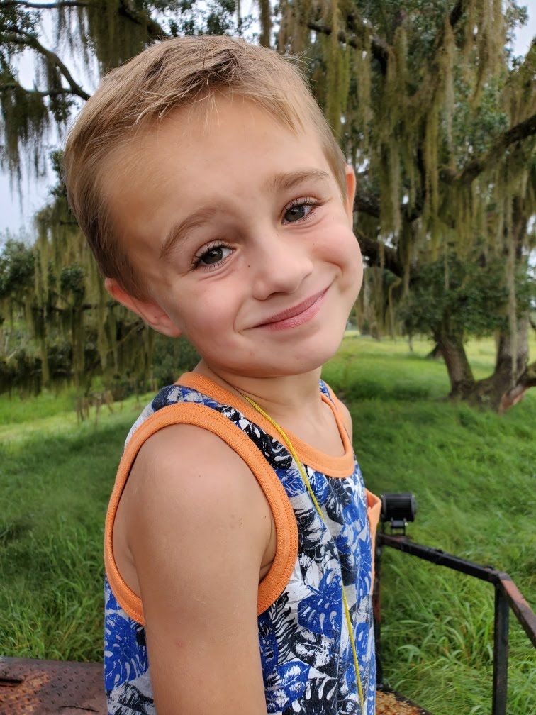 A young boy in a tank top is smiling in a field.