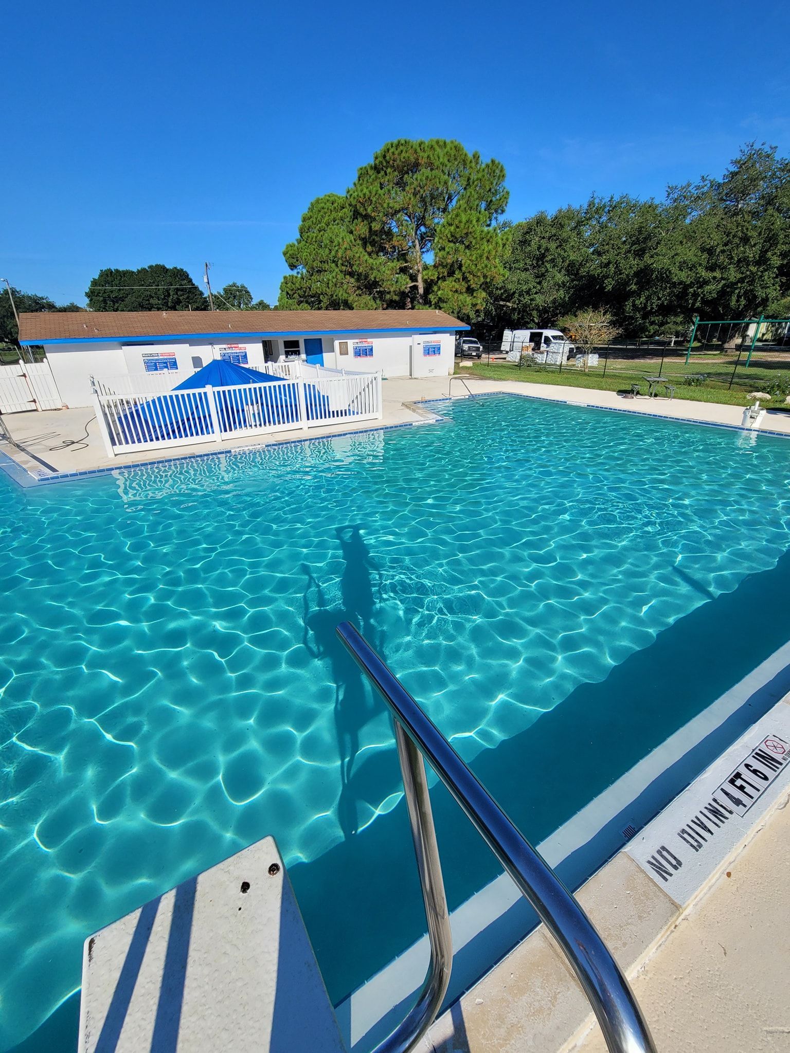 A large swimming pool with stairs leading to it and a house in the background.