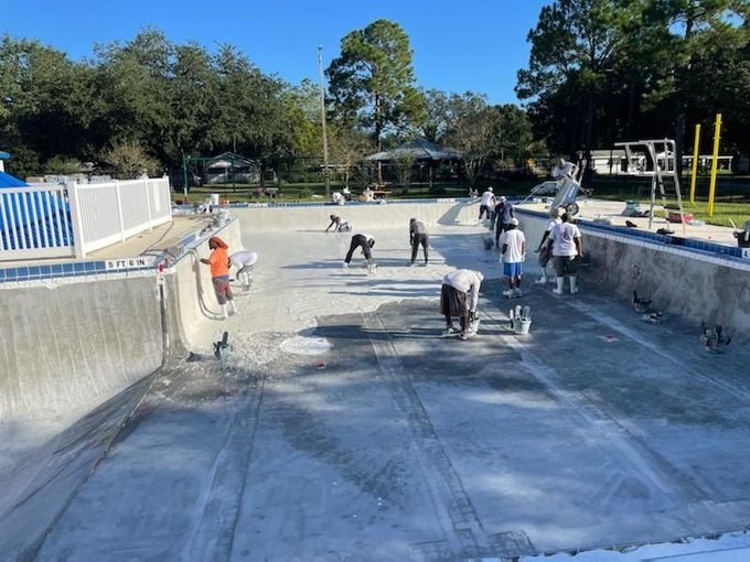 Workers renovating a drained swimming pool; applying material to the floor and walls. Outdoor, sunny day.