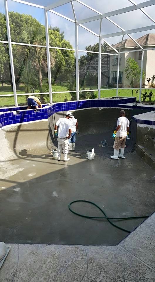 Pool being worked on by three people. Workers in white painting, cleaning, and repairing a pool.