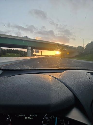 Sun setting on highway under a bridge, viewed from inside a vehicle.