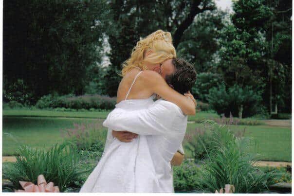 A bride and groom kissing in a park with trees in the background