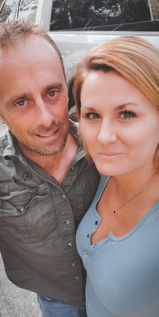 A man and a woman are posing for a selfie in front of a car.