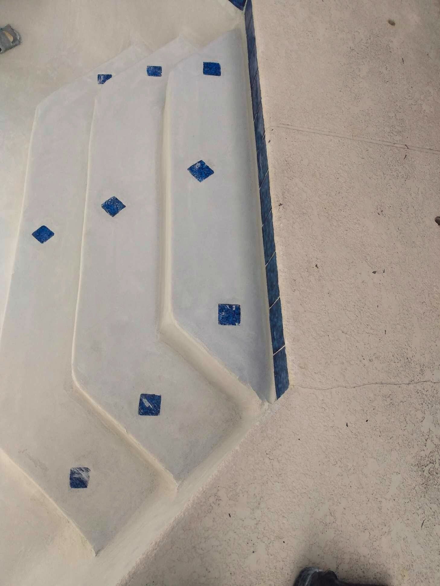 A white staircase with blue squares on it is next to a pool.