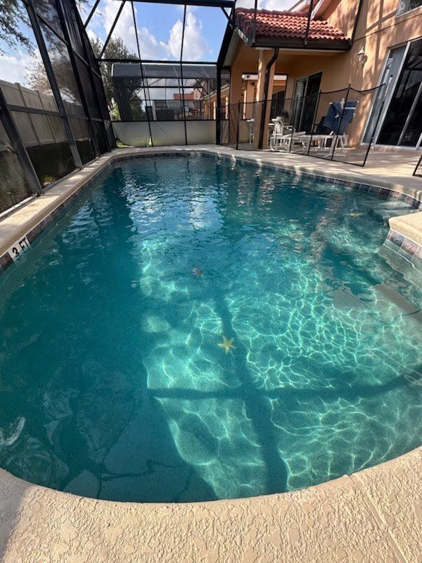 Pool with clear turquoise water enclosed by a screen. A house and furniture are visible in the background.