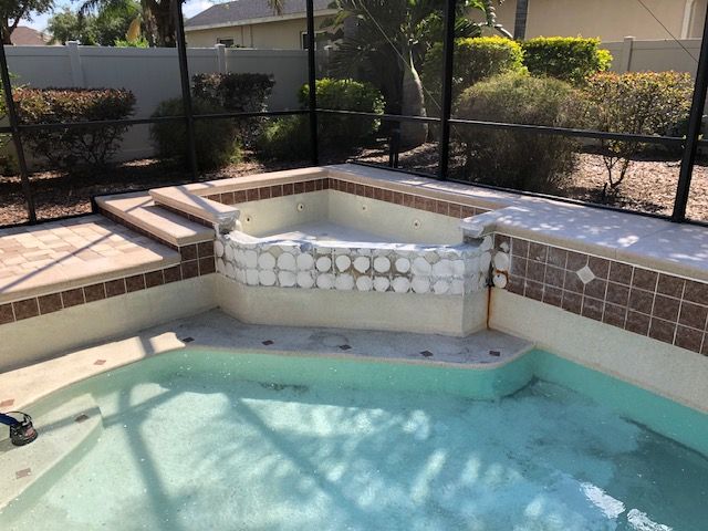 Swimming pool with attached spa, surrounded by a screened enclosure and tile border.