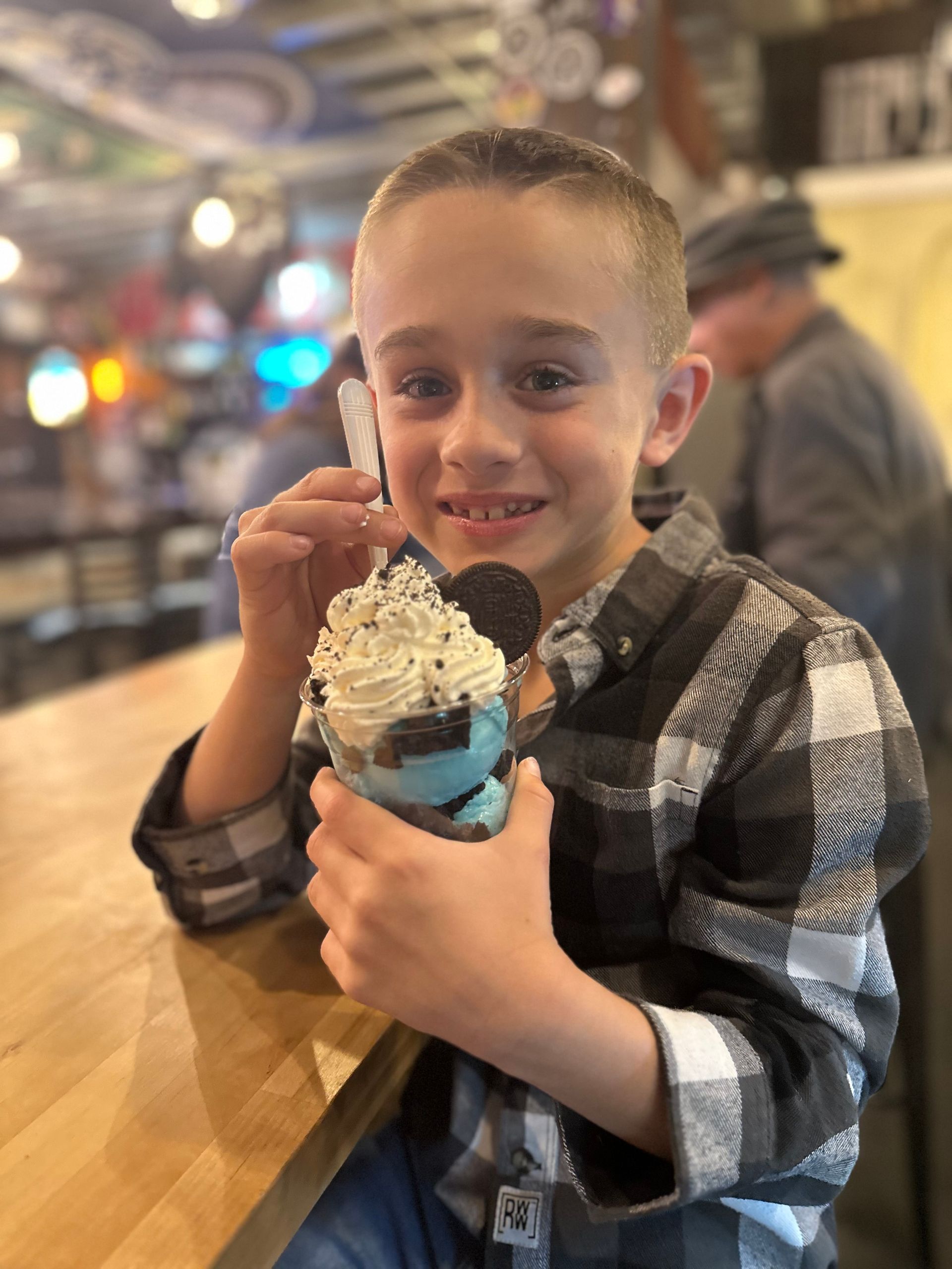 A young boy is sitting at a table eating ice cream.