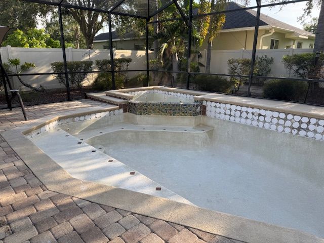 Empty swimming pool with a connected spa, surrounded by a brick patio and a black mesh enclosure.