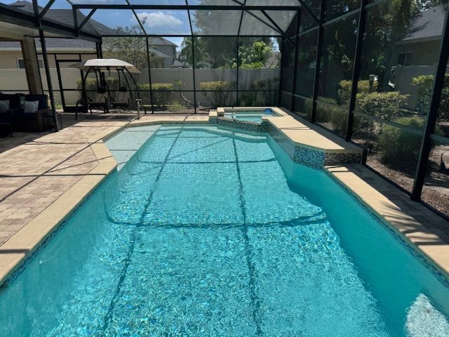 Swimming pool enclosed in a screened patio, with a hot tub, and surrounding patio.