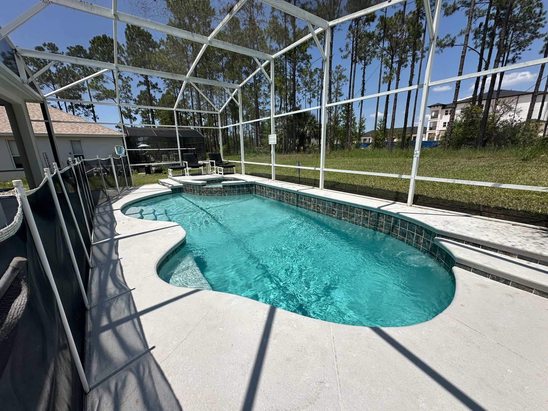 Pool enclosed in white screened cage, with turquoise water and concrete deck. Trees in background.