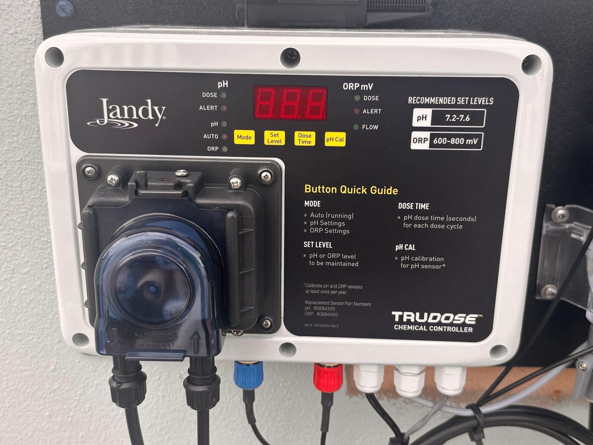 Jandy TruDose pool automation system with digital display, buttons, and chemical pump, mounted on a wall.