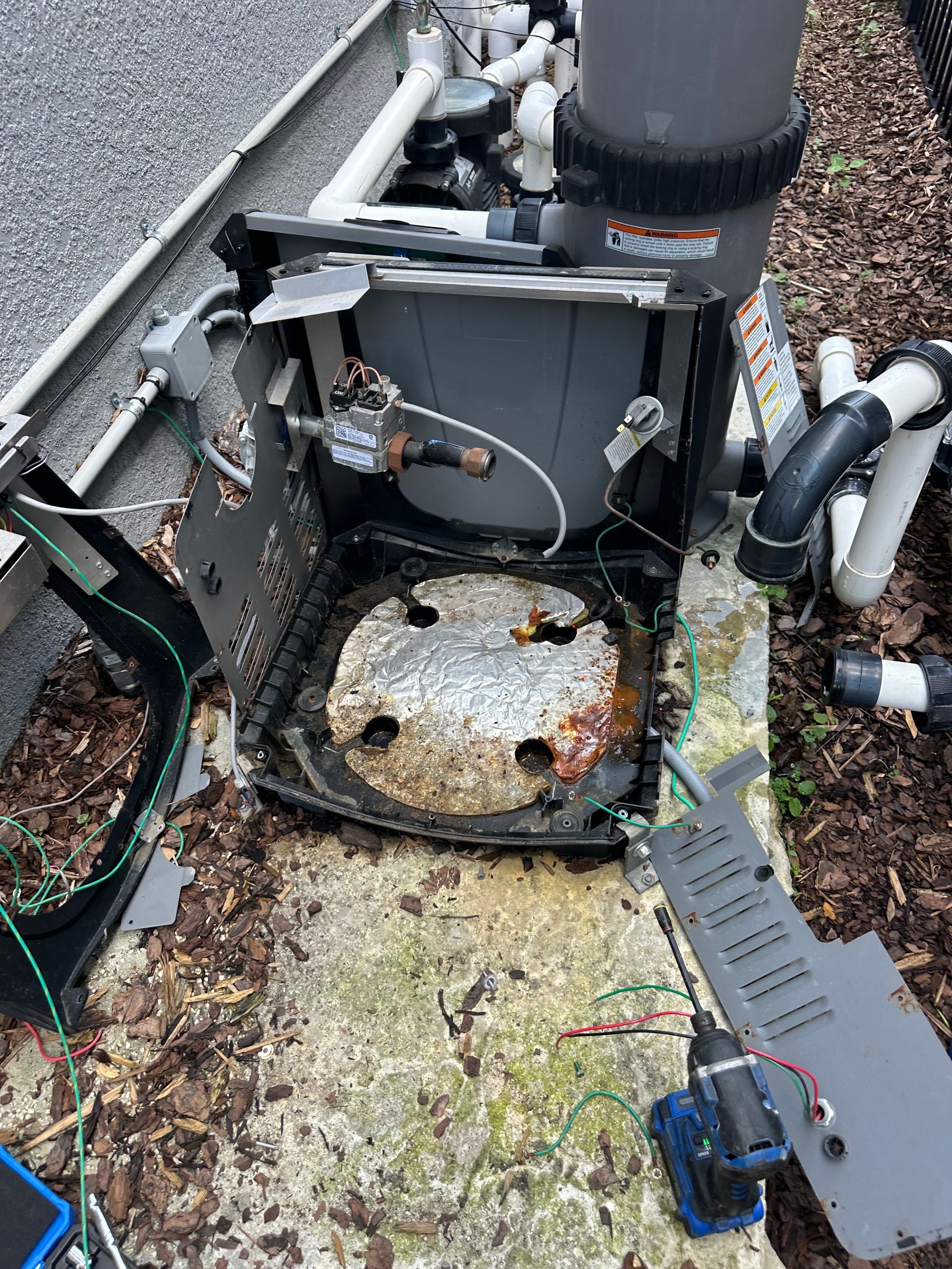 A broken water heater is sitting on the ground next to a fence.