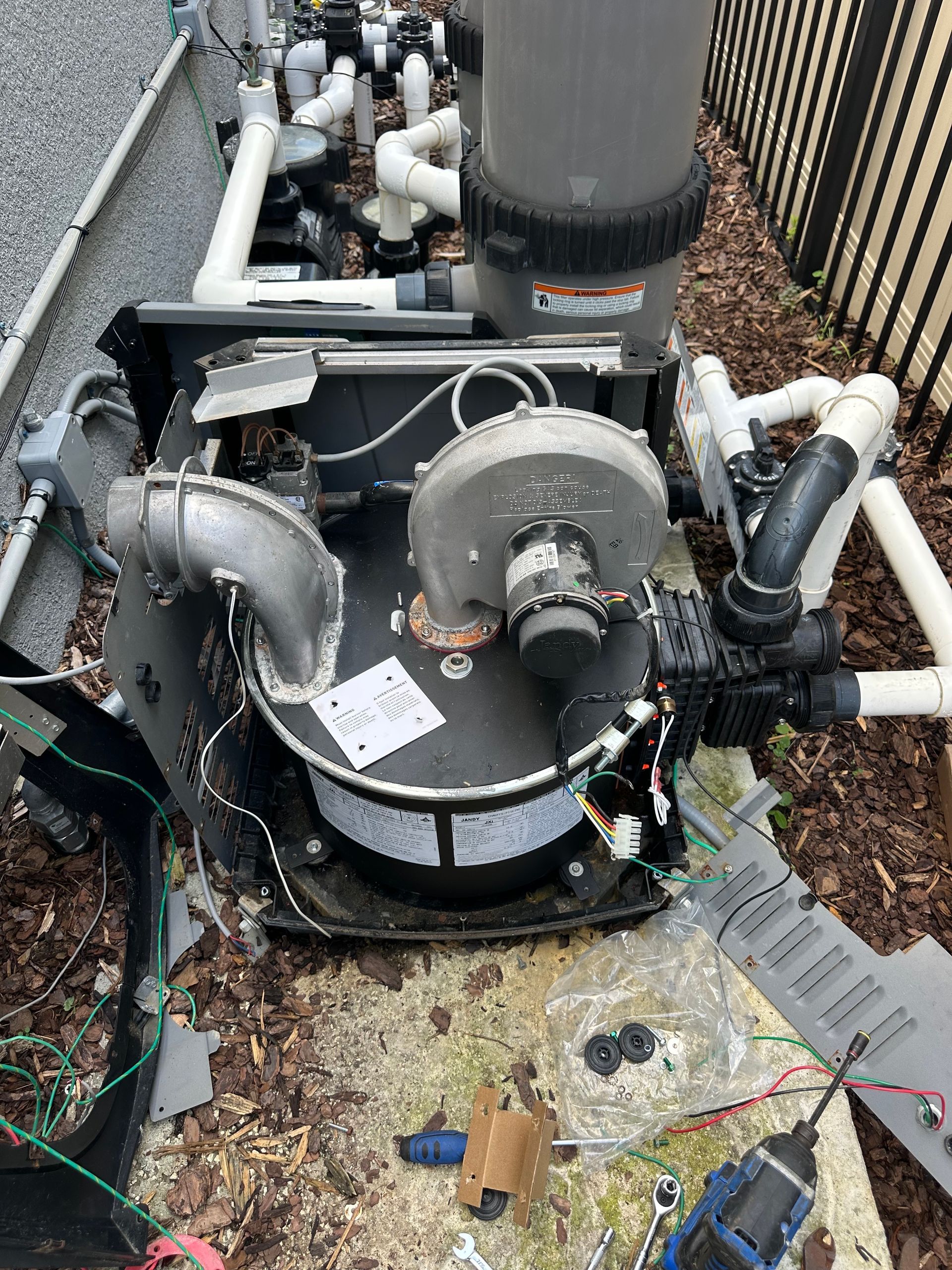 A pool pump is sitting on the ground next to a fence.