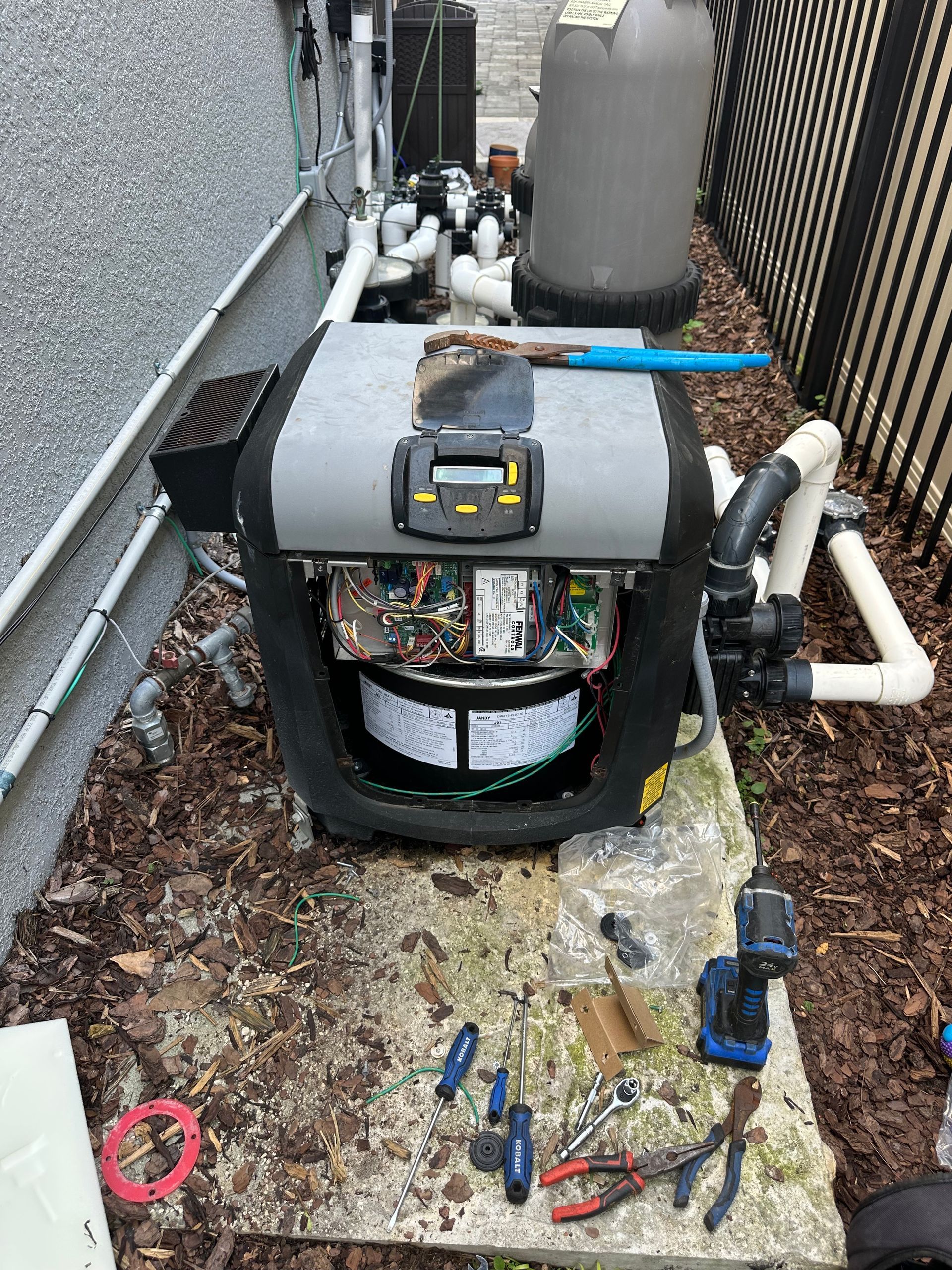 A pool heater is sitting on top of a wooden table next to a fence.