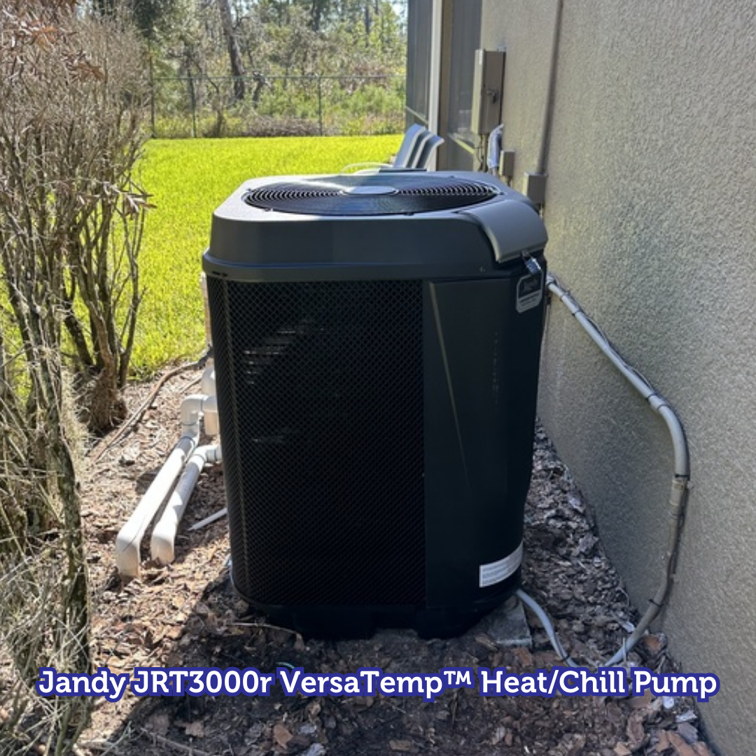 Jandy JRT3000r VersaTemp heat/chill pump beside a wall and bushes outdoors.
