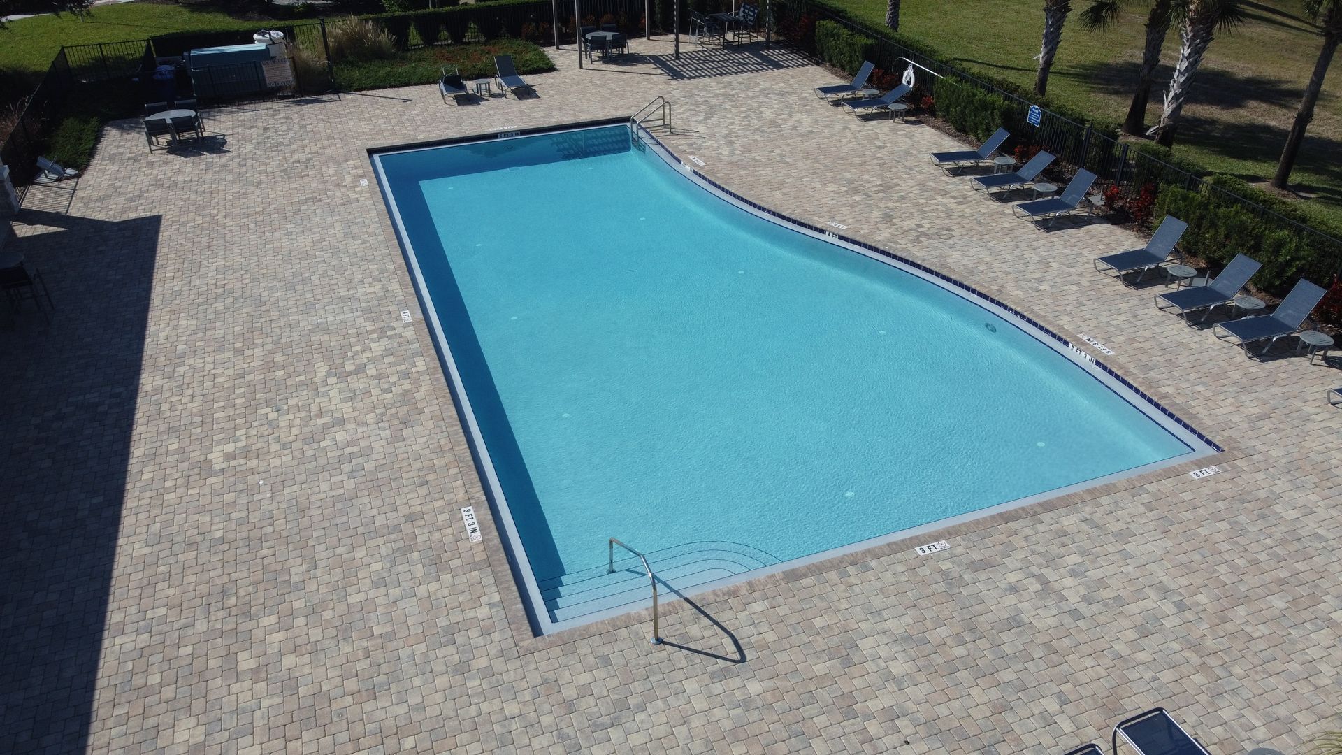 Outdoor swimming pool surrounded by brick patio and lounge chairs.