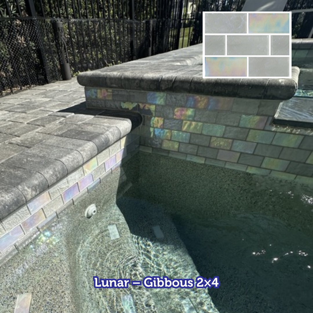 Pool edge with iridescent 2x4 tiles, surrounded by a gray stone coping. Water reflects light.