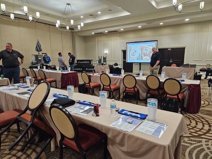 Conference room with attendees, presentation on screen, tables with materials, and chairs.