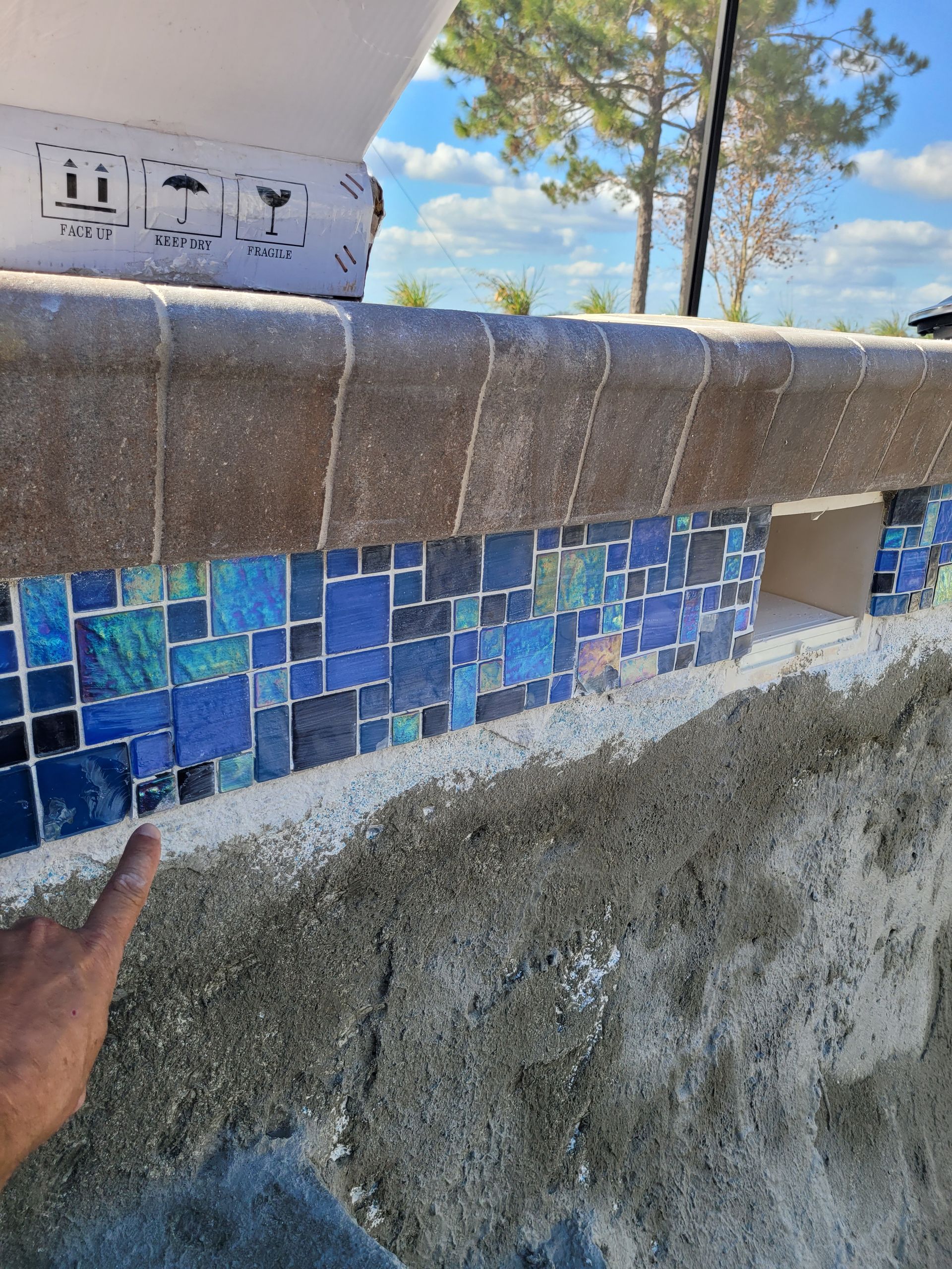 A person is pointing at a wall with blue tiles on it.
