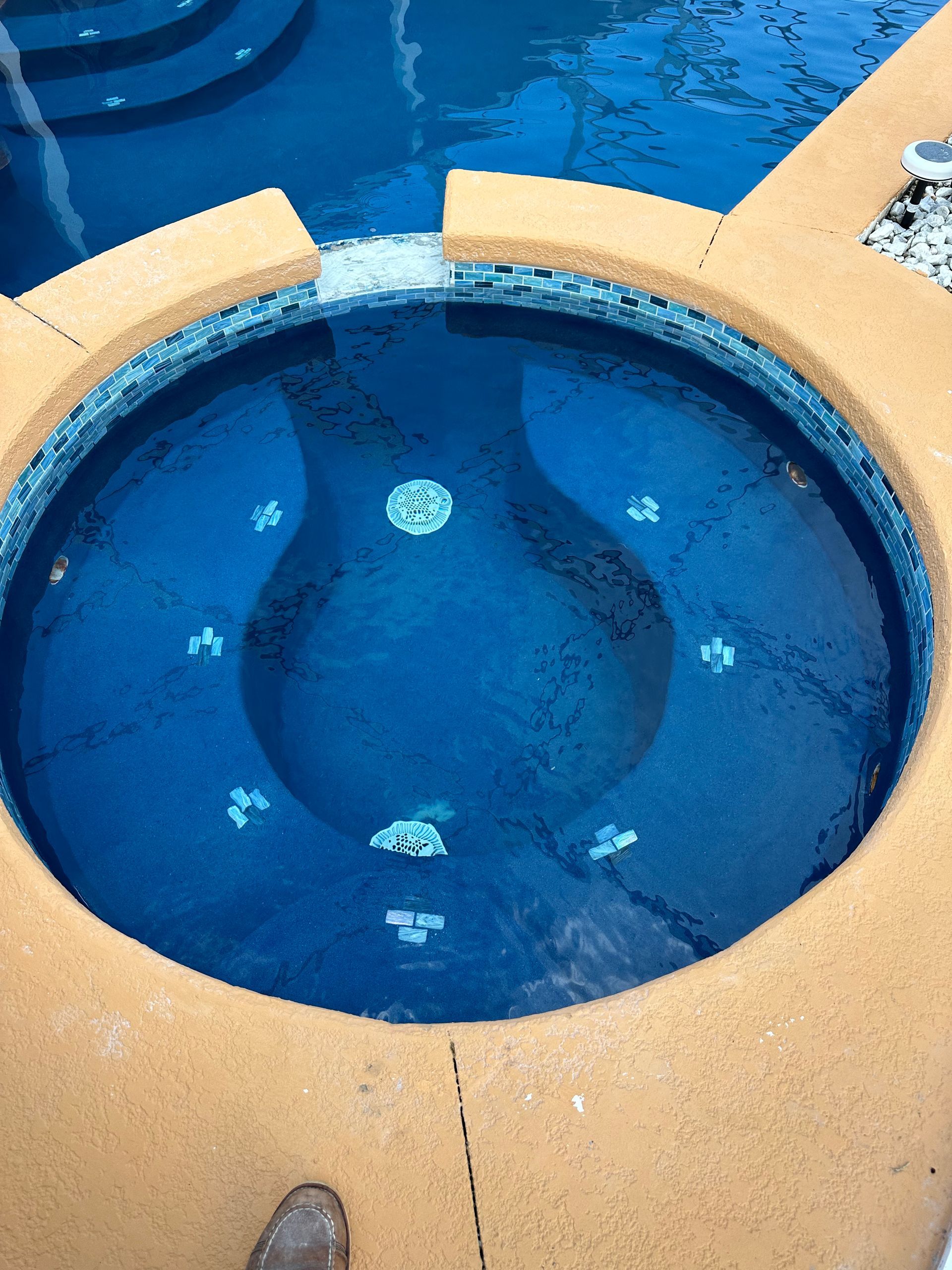 A circular jacuzzi with blue tile and jets, surrounded by tan concrete, adjacent to a blue pool.