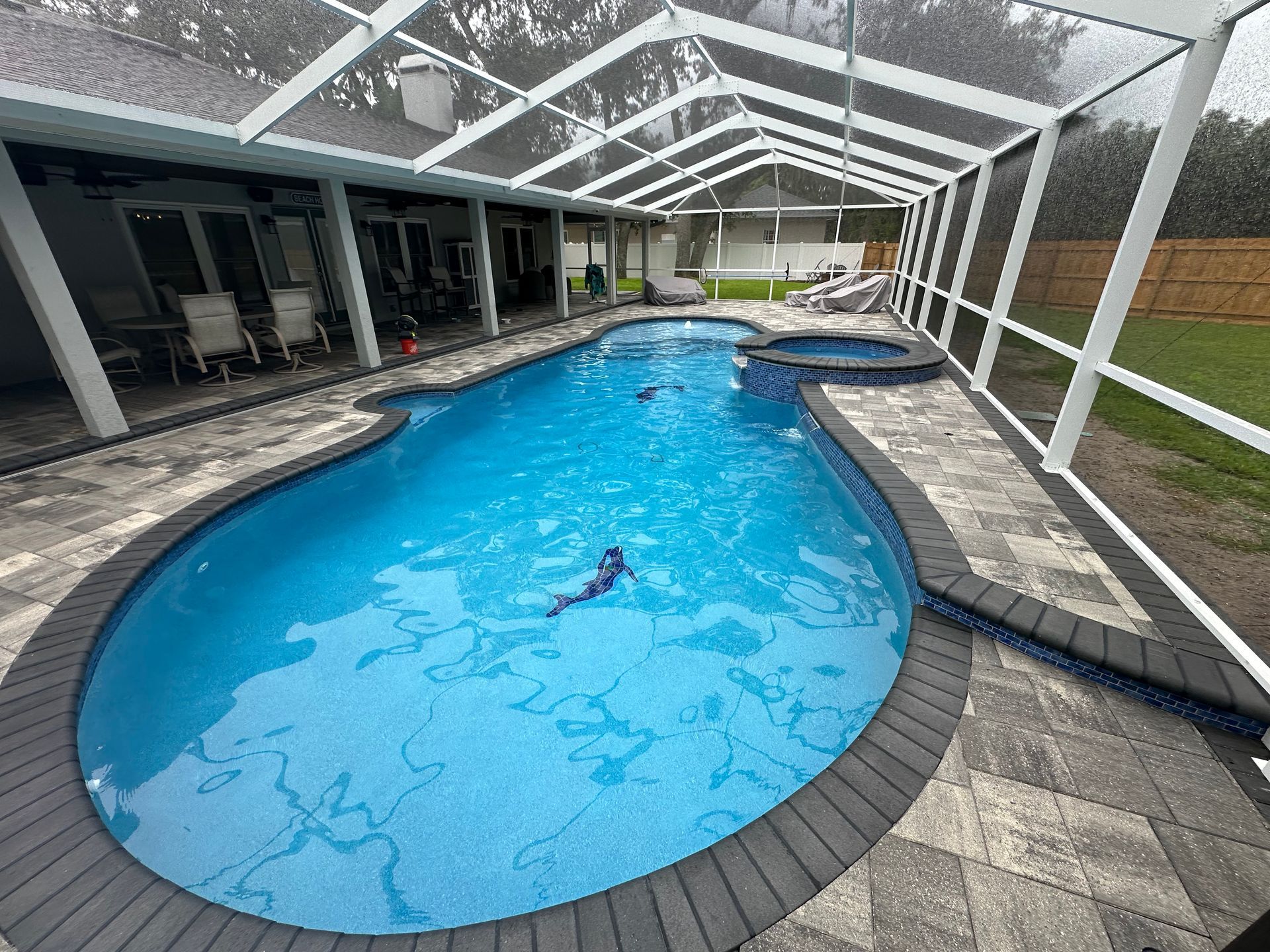 A person is swimming in a large swimming pool under a screened in area.
