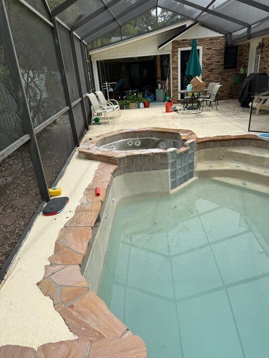 Pool area with spa, screen enclosure, and house in the background. Light blue water.