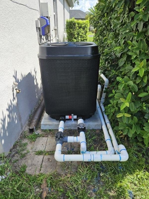 A pool heater is sitting on the side of a house next to some pipes.