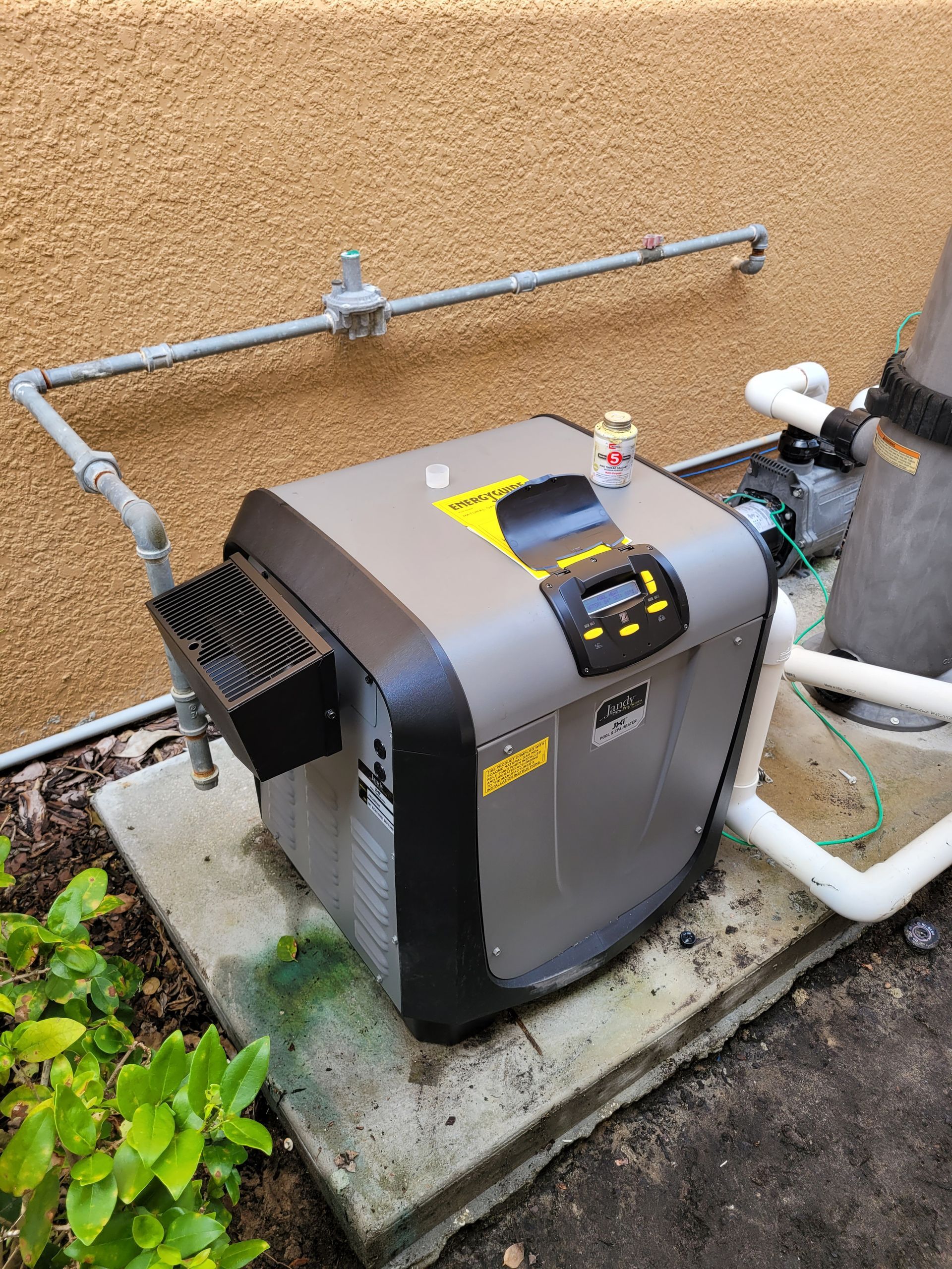 A pool heater is sitting on top of a concrete slab next to a wall.