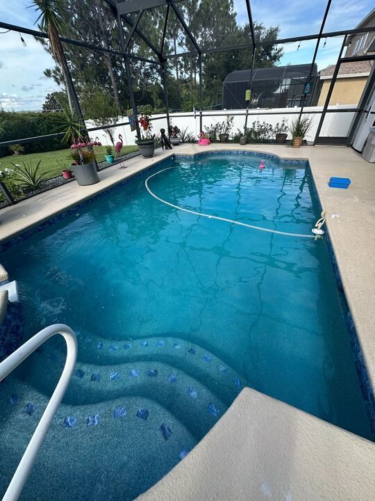 Pool with blue water and steps, surrounded by a screened patio and potted plants.