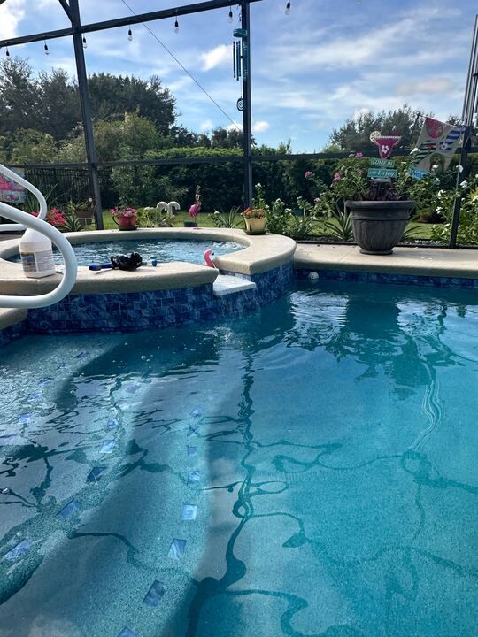 Blue-tiled swimming pool and spa surrounded by a patio, overlooking greenery under a partly cloudy sky.