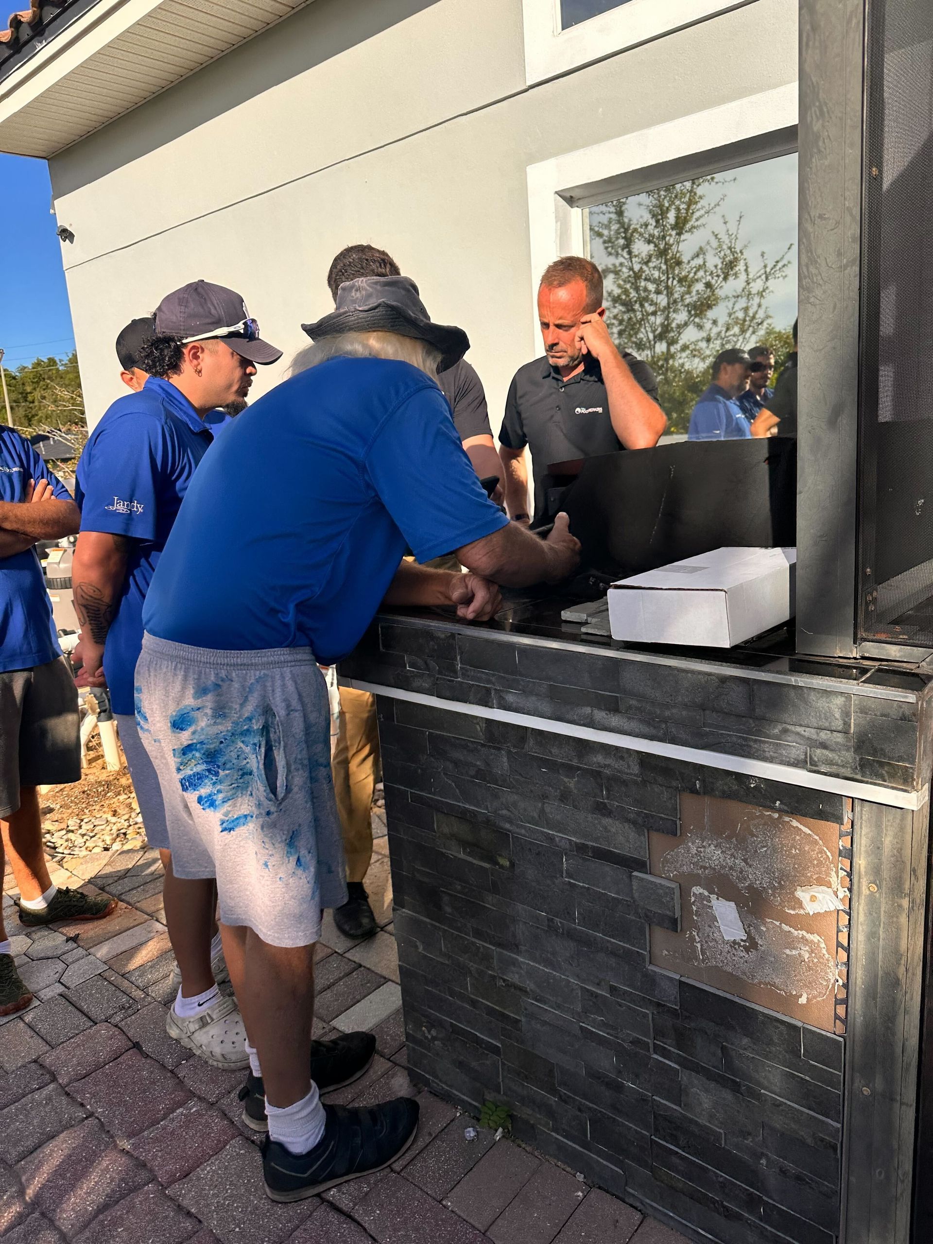 Group of men in blue shirts at a counter, one on the phone, likely at a construction site.