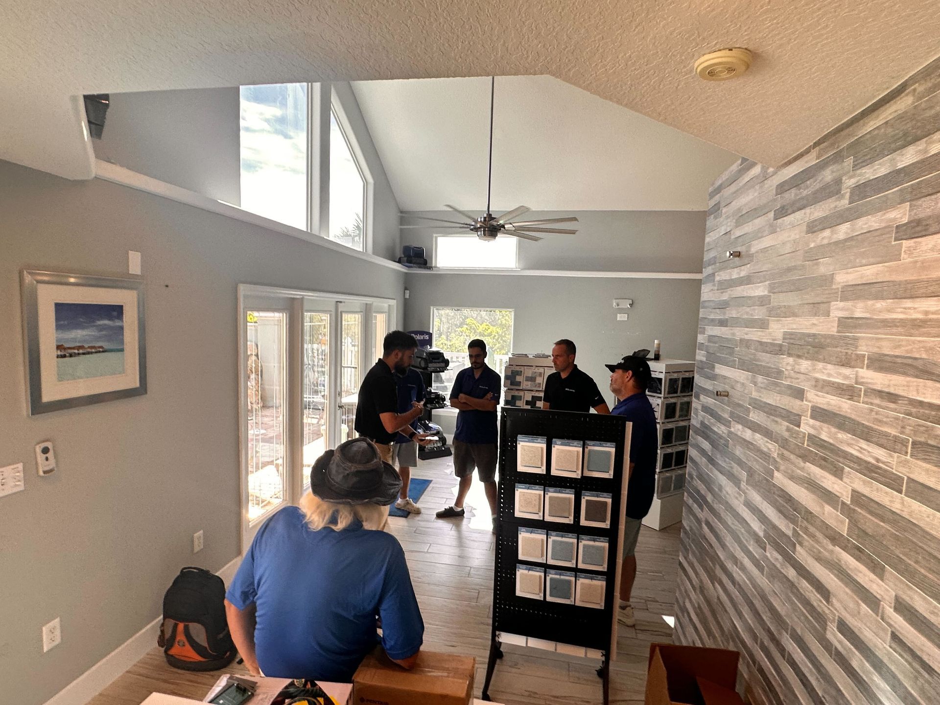 People discussing tile samples in a modern room with high ceilings. Some stand, others seated.