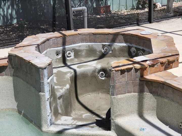 Empty built-in hot tub with dark jets and brick surround, near pool and fence.