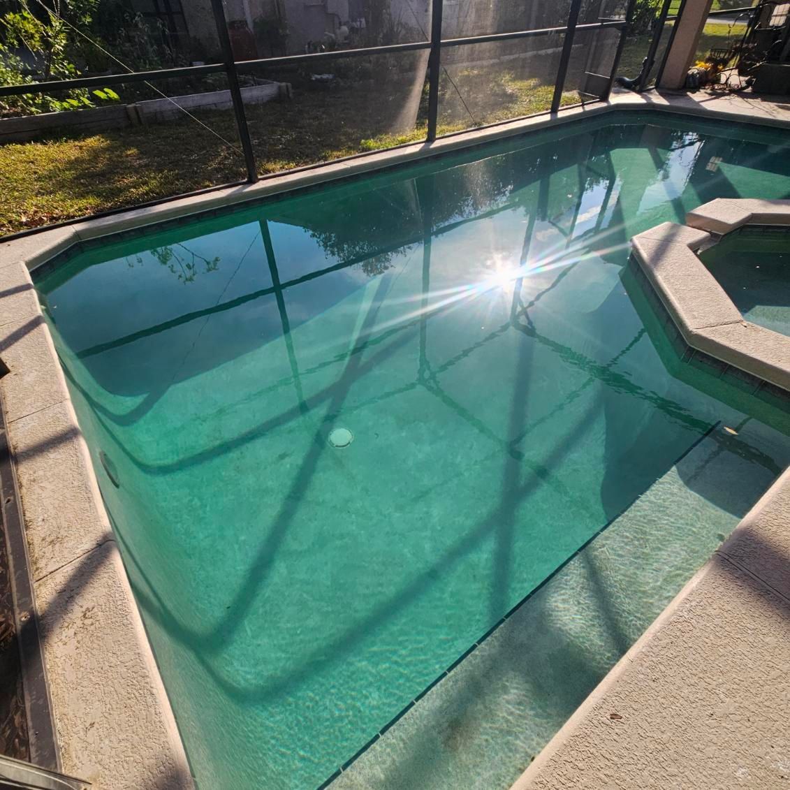 A swimming pool with clear turquoise water and a sunlit reflection surrounded by a concrete deck.