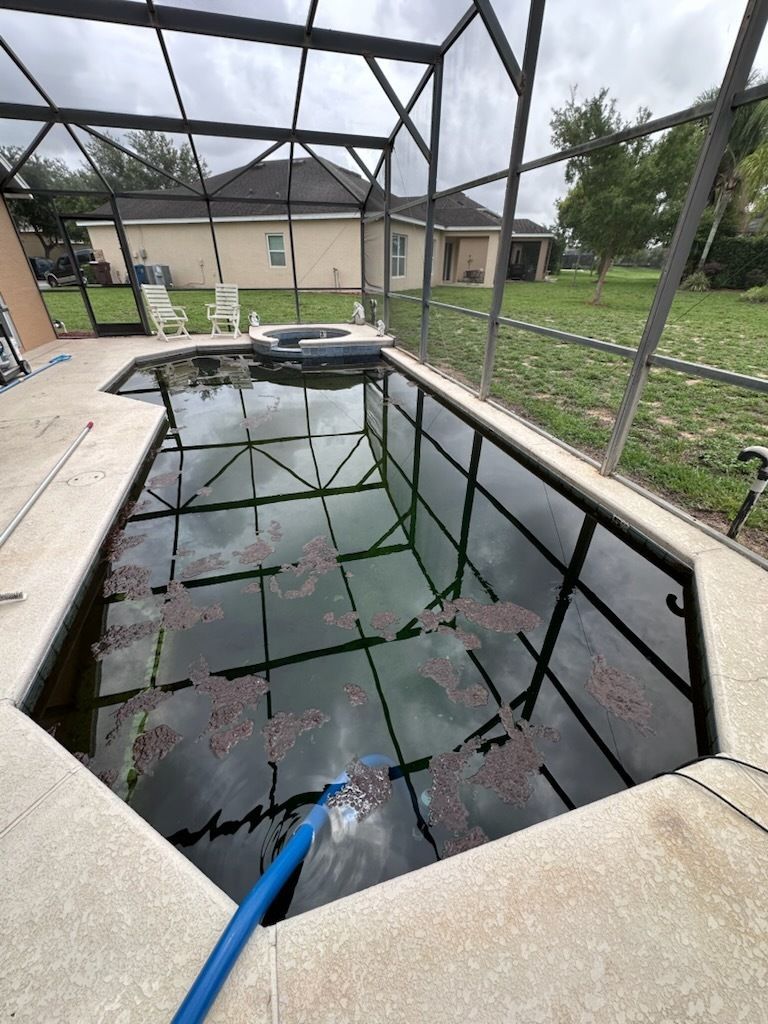 A swimming pool with a hose in it and a house in the background.