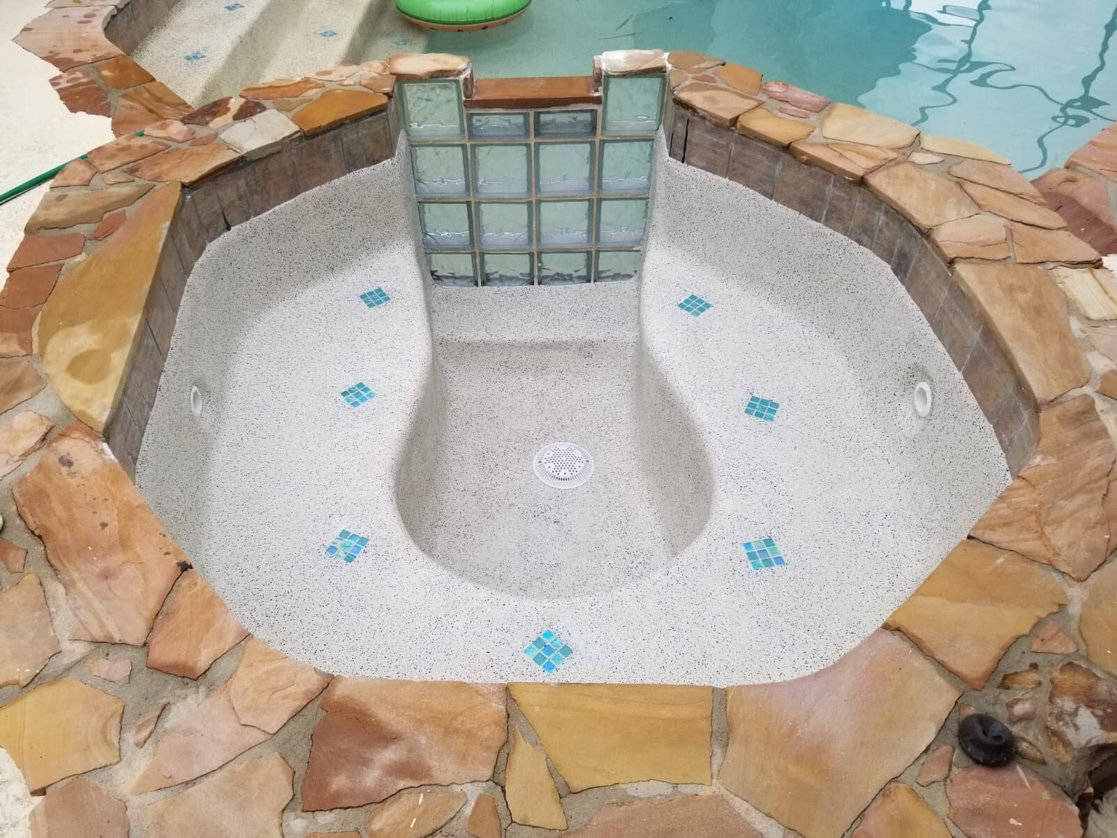 Empty hot tub with stone surround, blue tile accents, and glass block waterfall.