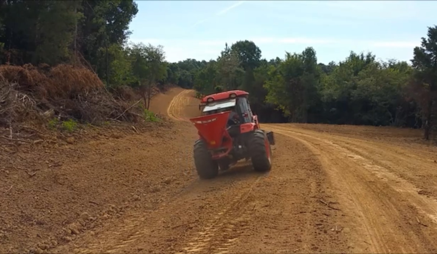 Person riding a small tractor plowing a field on a sunny, rolling hillside.