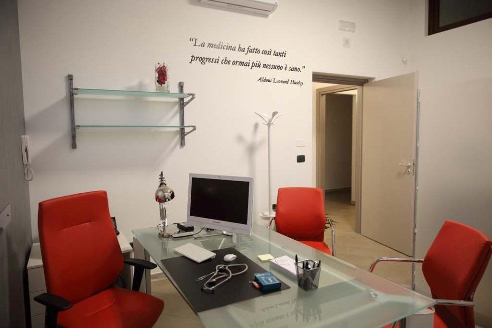 una scrivania in vetro con un monitor, uno stetoscopio e accanto delle sedie rosse