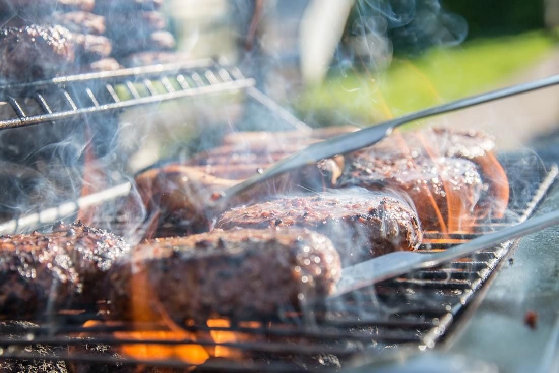 Meat grilling on a barbecue with smoke rising and tongs turning the food