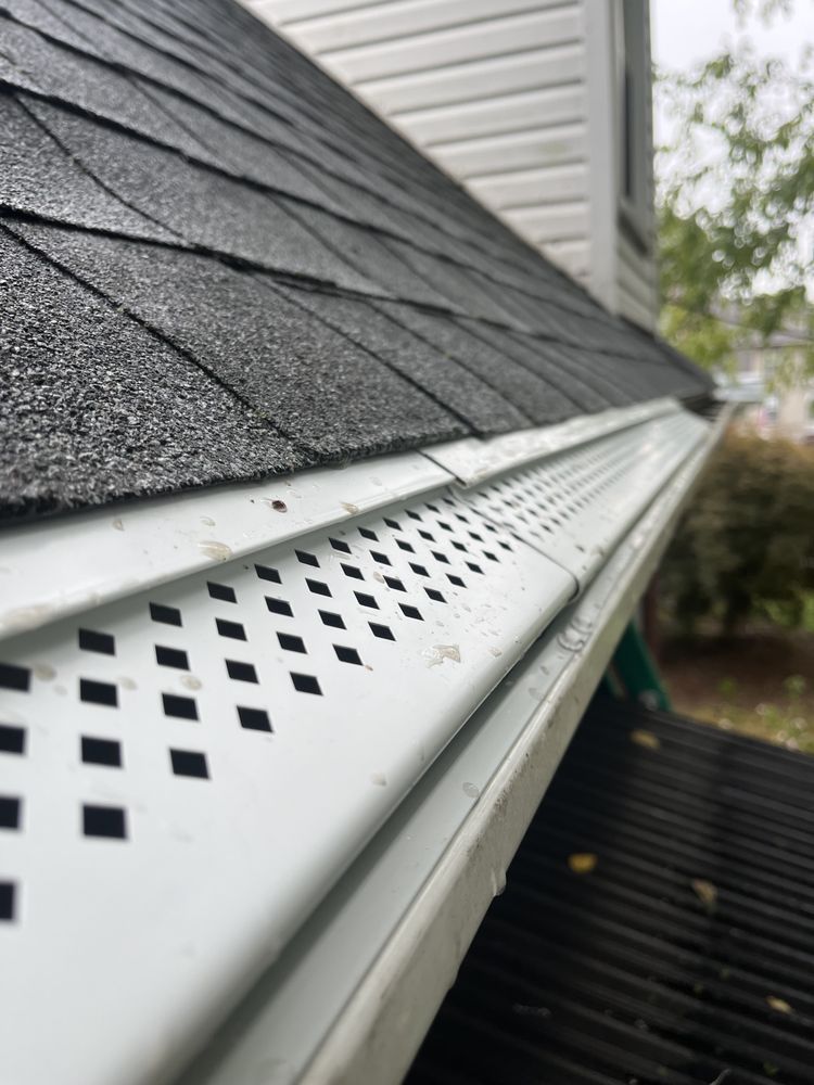 Close-up of white roof gutter with vented soffit beneath dark gray shingles on a house