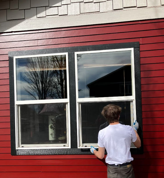 Person cleaning a red house window with a black frame and white trim