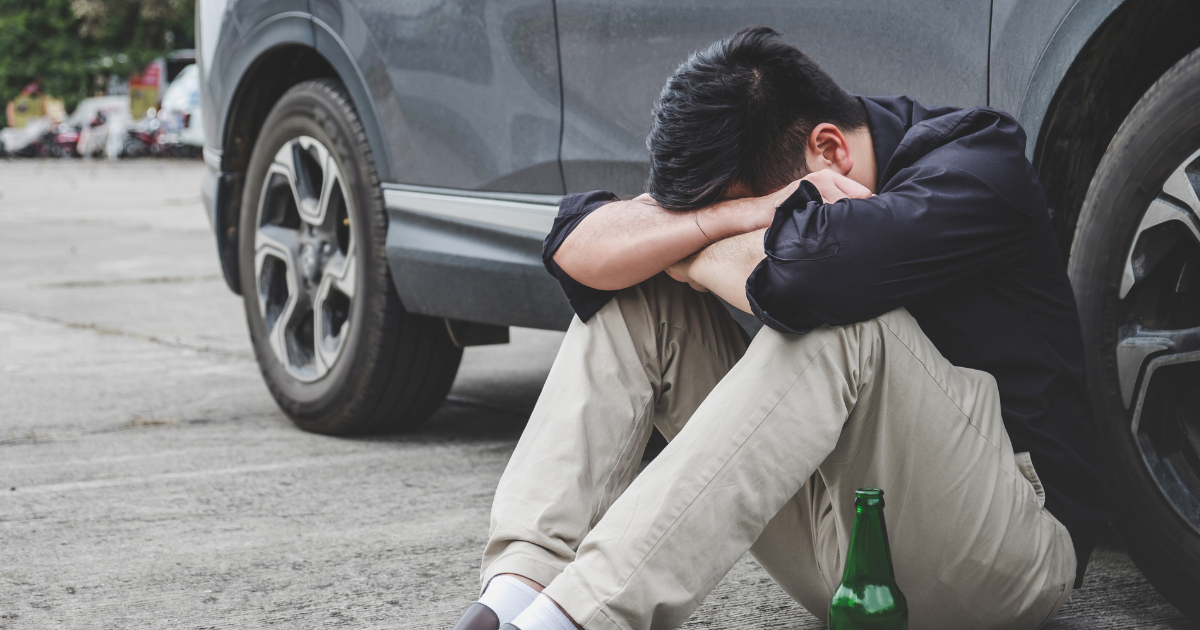 A man is sitting on the ground next to a car with his head in his hands. 