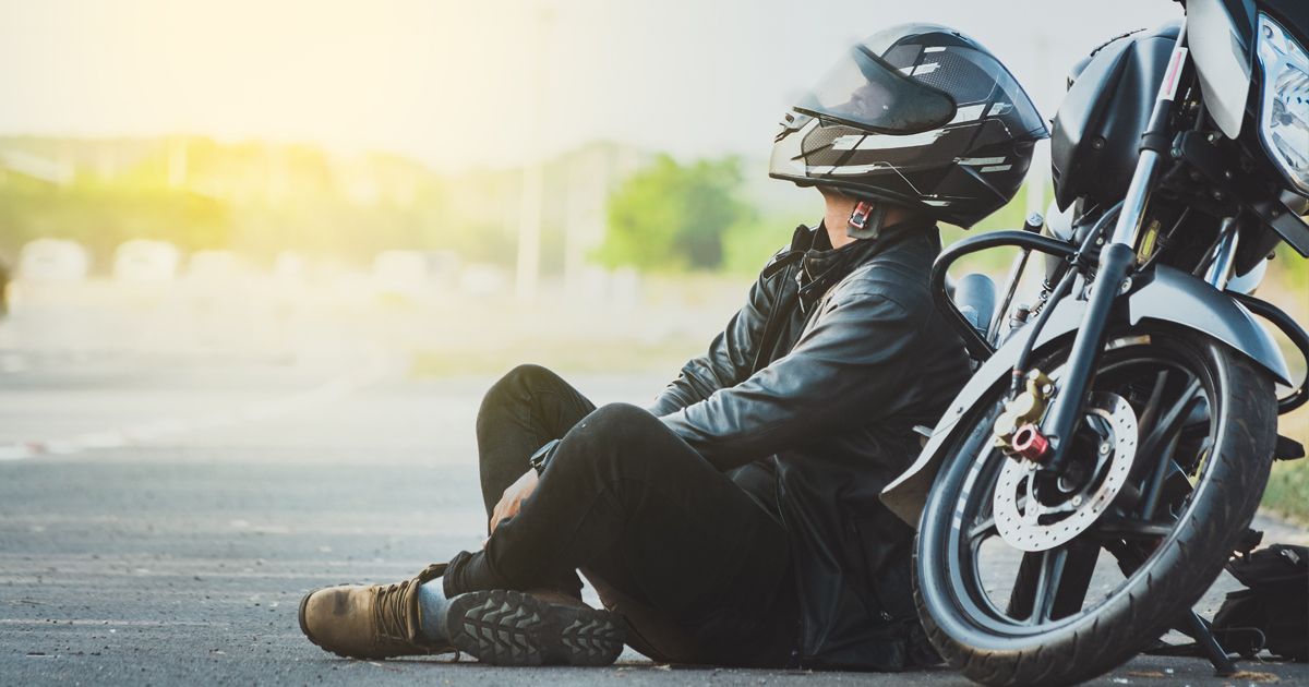 Motorcyclist seated on the roadside beside a black sport bike at sunset