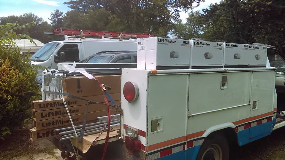 A white work truck loaded with LiftMaster garage door openers and equipment, parked outside.
