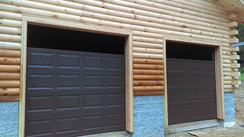 Two brown garage doors on a log cabin, against a blue stone base.